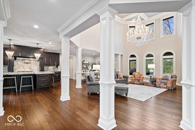 living room featuring an inviting chandelier, ornamental molding, dark wood-type flooring, and decorative columns