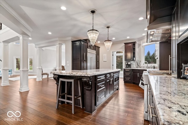 kitchen with a chandelier, decorative columns, ornamental molding, dark wood-type flooring, and a center island