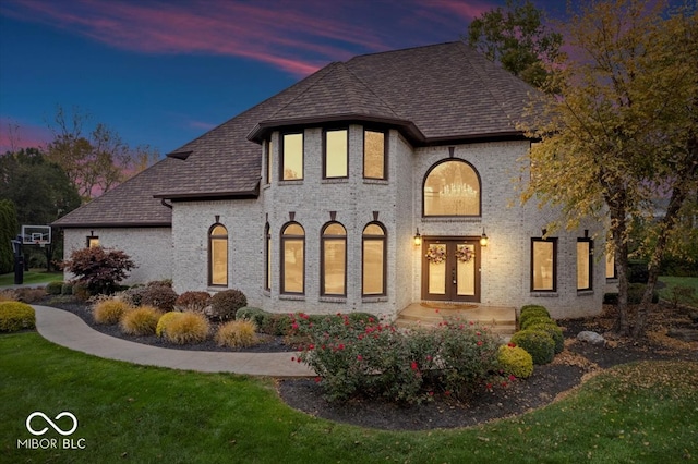 back house at dusk featuring french doors and a yard