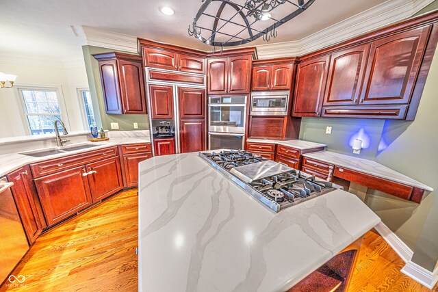 kitchen with light stone counters, crown molding, built in appliances, sink, and light hardwood / wood-style flooring