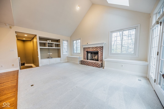 unfurnished living room with a brick fireplace, high vaulted ceiling, light hardwood / wood-style flooring, and a skylight