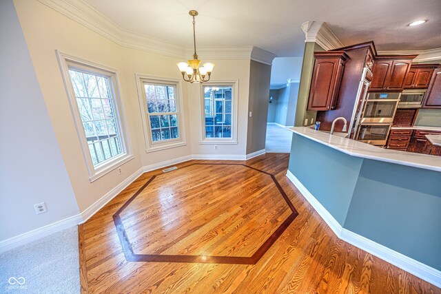 kitchen with stainless steel appliances, wood-type flooring, a chandelier, crown molding, and decorative light fixtures