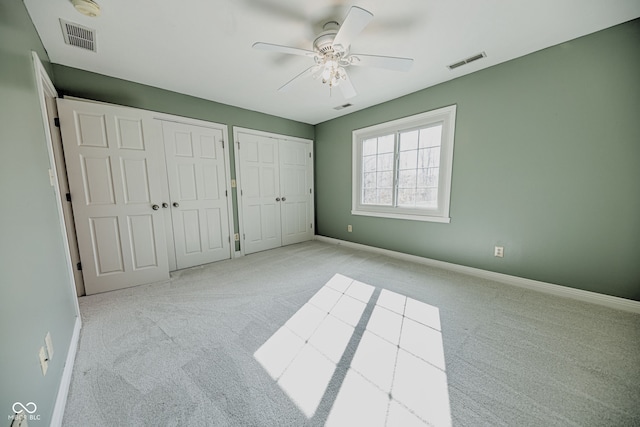 unfurnished bedroom with two closets, light carpet, and ceiling fan