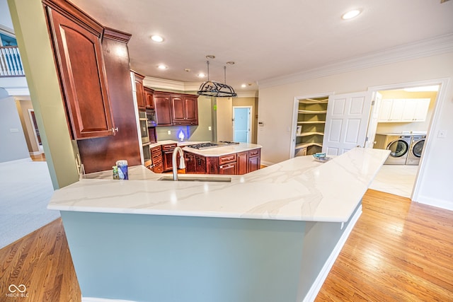 kitchen featuring a kitchen island with sink, hanging light fixtures, sink, washer and dryer, and light hardwood / wood-style flooring