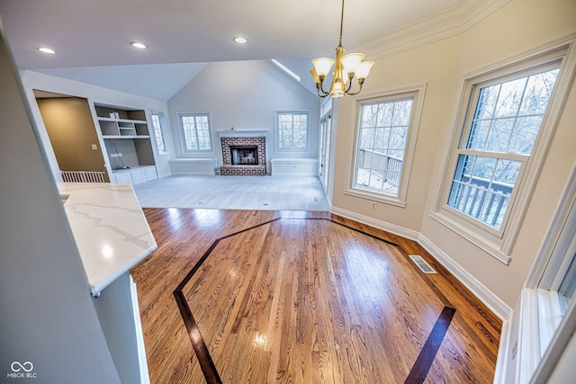 808 Copperfield Xing, Danville, IN 46122 - unfurnished living room featuring wood finished floors, vaulted ceiling, built in shelves, a brick fireplace, and a chandelier