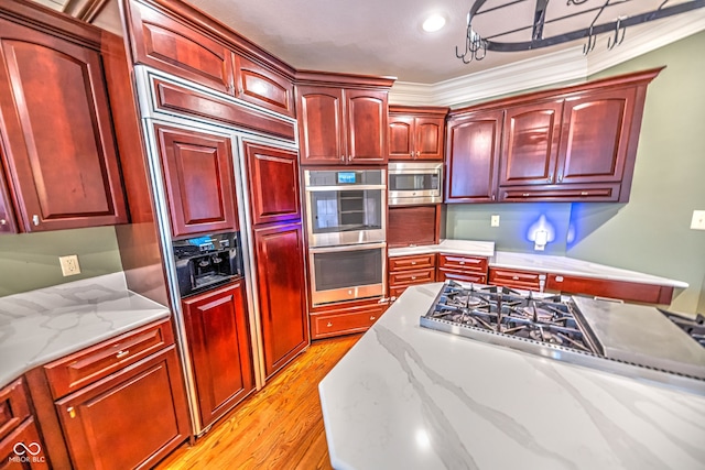 kitchen featuring light stone countertops, crown molding, built in appliances, and light hardwood / wood-style flooring