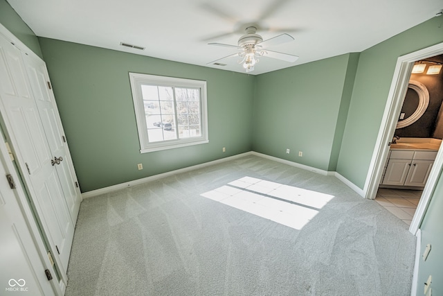 unfurnished bedroom featuring sink, light colored carpet, ceiling fan, and ensuite bathroom