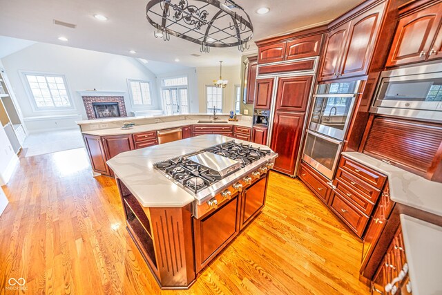 kitchen featuring decorative light fixtures, built in appliances, a brick fireplace, kitchen peninsula, and light hardwood / wood-style flooring