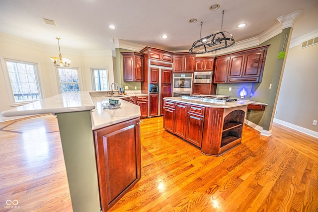 kitchen featuring light wood-type flooring, kitchen peninsula, an inviting chandelier, and built in appliances