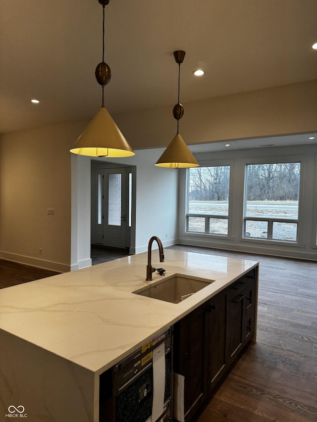 kitchen featuring pendant lighting, an island with sink, sink, dark hardwood / wood-style flooring, and light stone counters