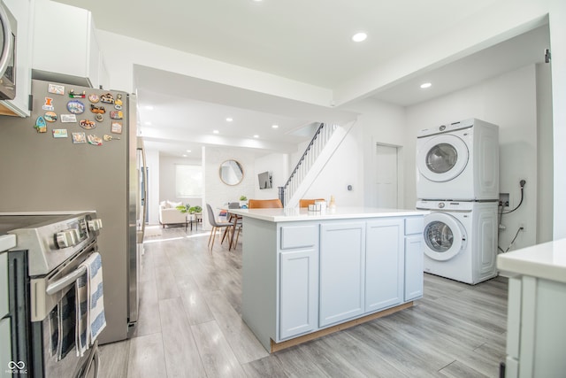 kitchen with stacked washer / drying machine, a center island, white cabinets, light wood-type flooring, and appliances with stainless steel finishes