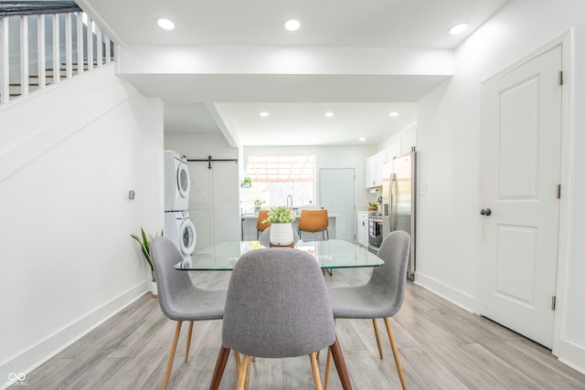 dining space featuring light hardwood / wood-style flooring, a barn door, and stacked washer and clothes dryer