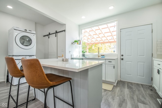 kitchen featuring stacked washing maching and dryer, sink, a barn door, white cabinets, and light hardwood / wood-style floors