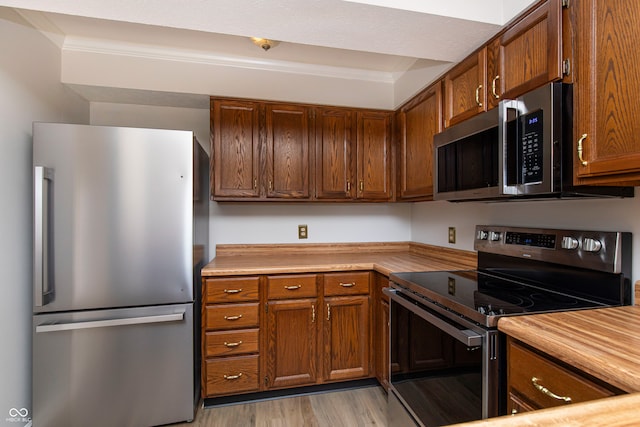 kitchen featuring ornamental molding, light hardwood / wood-style flooring, and stainless steel appliances