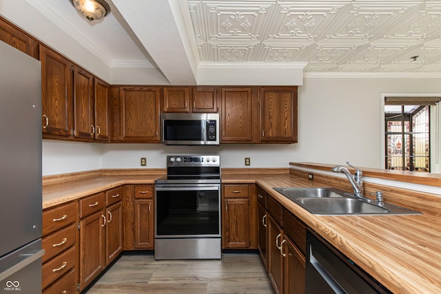 kitchen featuring butcher block counters, light hardwood / wood-style flooring, sink, crown molding, and appliances with stainless steel finishes