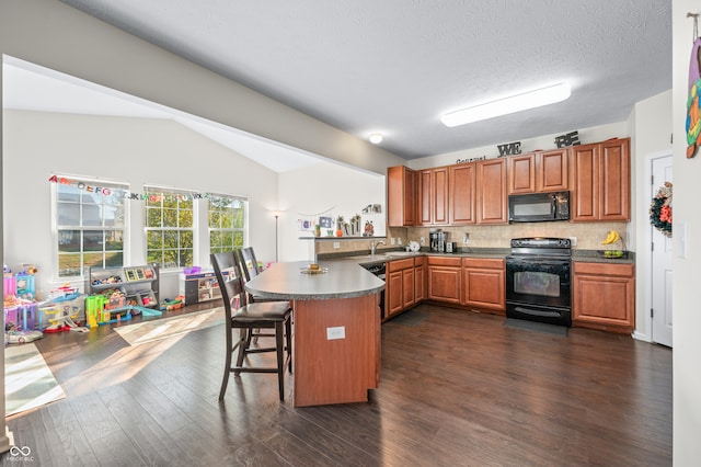 kitchen featuring dark wood-type flooring, kitchen peninsula, backsplash, black appliances, and a breakfast bar