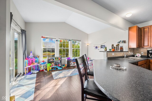 kitchen with lofted ceiling, kitchen peninsula, backsplash, hardwood / wood-style floors, and sink