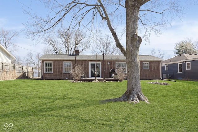 rear view of house with a yard, brick siding, a chimney, and fence