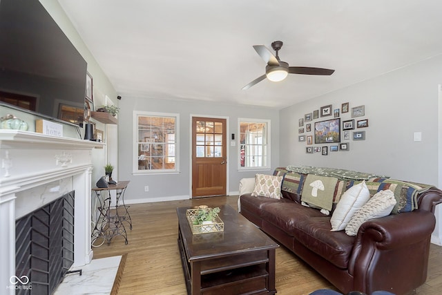 living area with baseboards, a fireplace with flush hearth, wood finished floors, and a ceiling fan