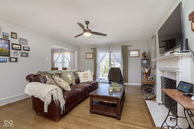 living area with light wood-style flooring, plenty of natural light, baseboards, and a fireplace with flush hearth