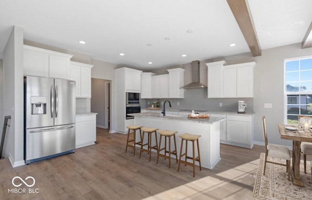 kitchen with a center island with sink, white cabinets, wall chimney range hood, black appliances, and a sink