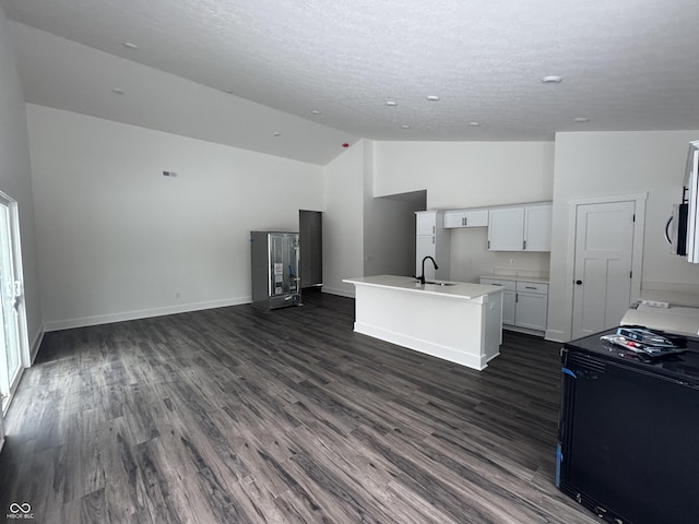 kitchen with sink, white cabinetry, vaulted ceiling, black stove, and a kitchen island with sink