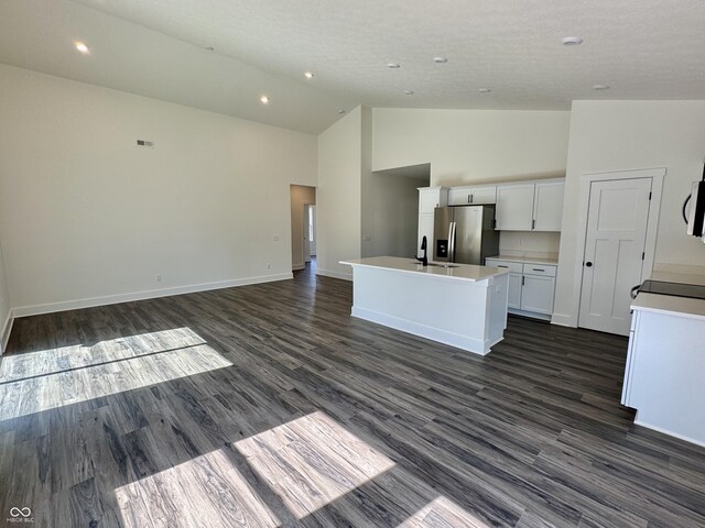 kitchen with baseboards, a center island with sink, dark wood-style floors, stainless steel fridge, and white cabinetry