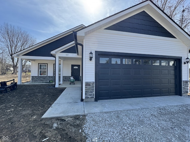 view of side of property with stone siding, an attached garage, a porch, and driveway