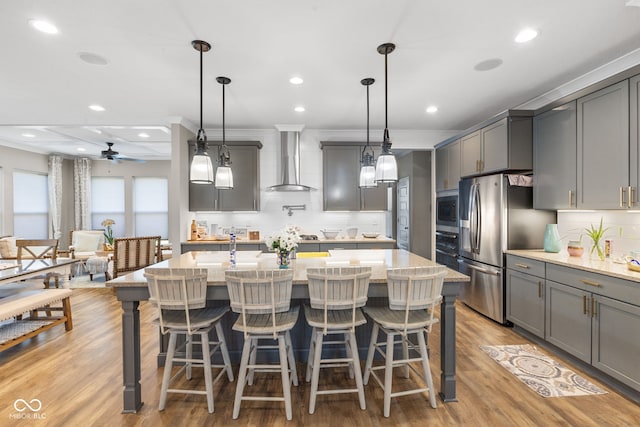 kitchen featuring wall chimney range hood, gray cabinets, light wood-type flooring, and hanging light fixtures