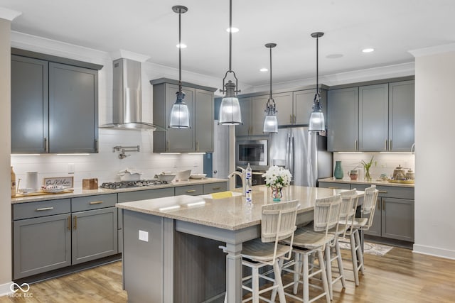 kitchen featuring wall chimney exhaust hood, a kitchen island with sink, hanging light fixtures, and stainless steel appliances