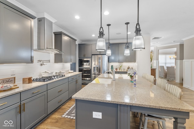 kitchen with wall chimney range hood, a kitchen island with sink, stainless steel appliances, and a kitchen bar