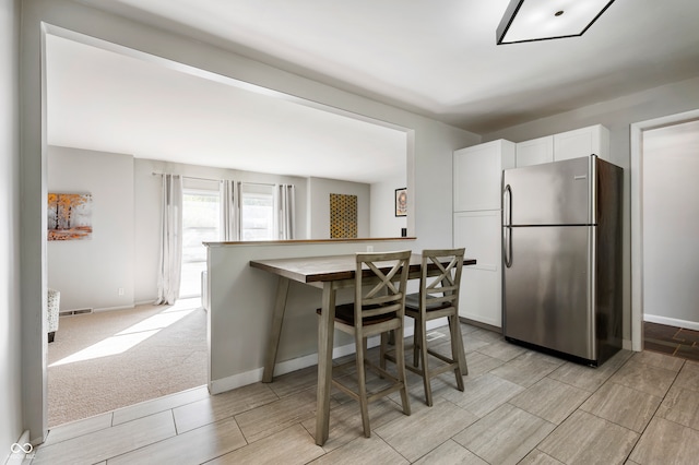 kitchen with a kitchen breakfast bar, white cabinetry, light colored carpet, and stainless steel refrigerator