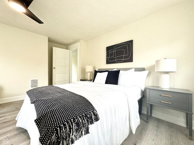 bedroom with light hardwood / wood-style flooring, a textured ceiling, and ceiling fan