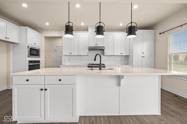 kitchen with decorative light fixtures, white cabinetry, a kitchen island with sink, and built in microwave