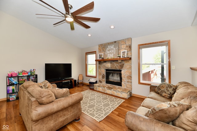 living room with ceiling fan, hardwood / wood-style flooring, lofted ceiling, and a stone fireplace