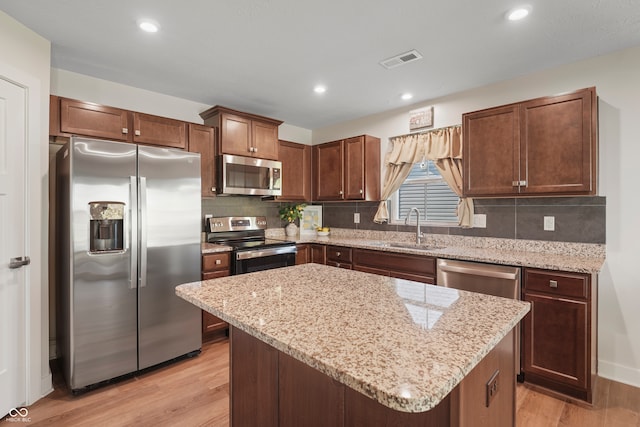 kitchen with stainless steel appliances, sink, light wood-type flooring, and a kitchen island