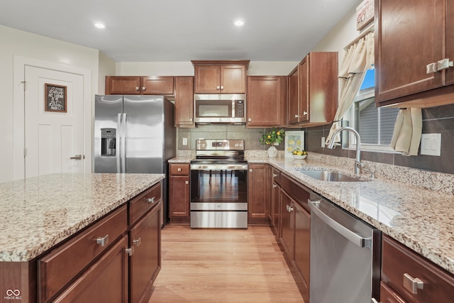 kitchen with light hardwood / wood-style floors, appliances with stainless steel finishes, sink, and light stone countertops