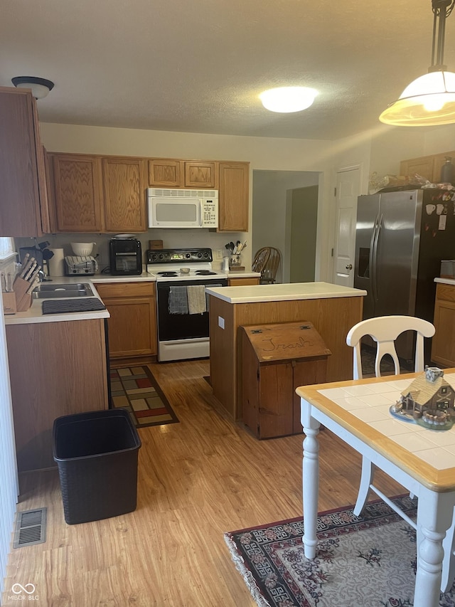 kitchen featuring white appliances, sink, decorative light fixtures, a center island, and light hardwood / wood-style floors