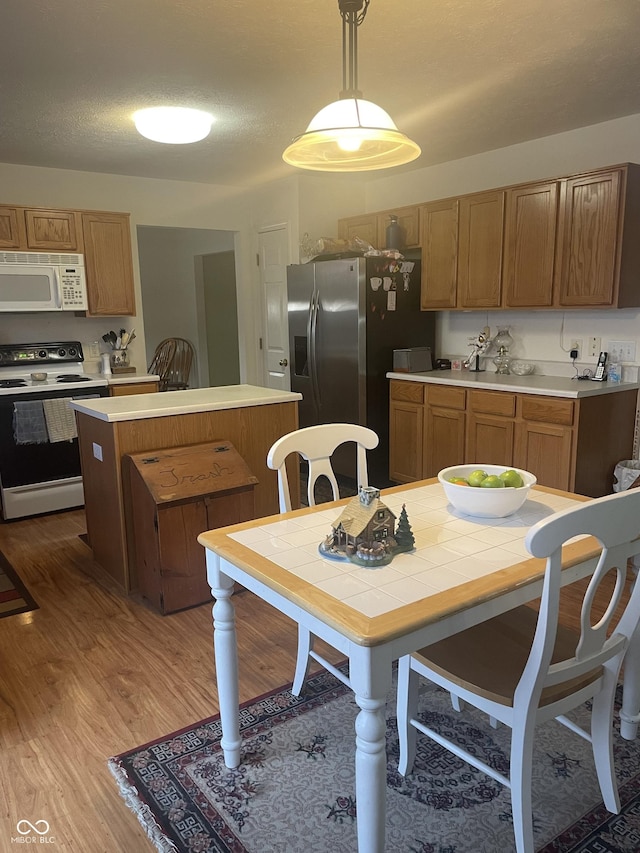 kitchen featuring hanging light fixtures, a textured ceiling, white appliances, a kitchen island, and hardwood / wood-style flooring