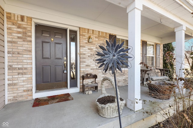 entrance to property featuring a porch and brick siding