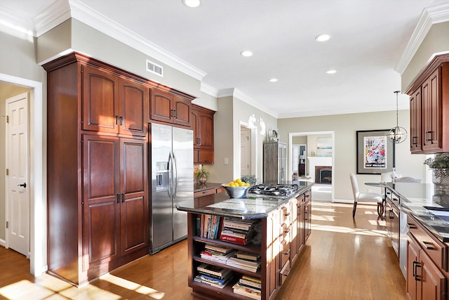 kitchen with decorative light fixtures, dark stone counters, light hardwood / wood-style floors, stainless steel appliances, and crown molding