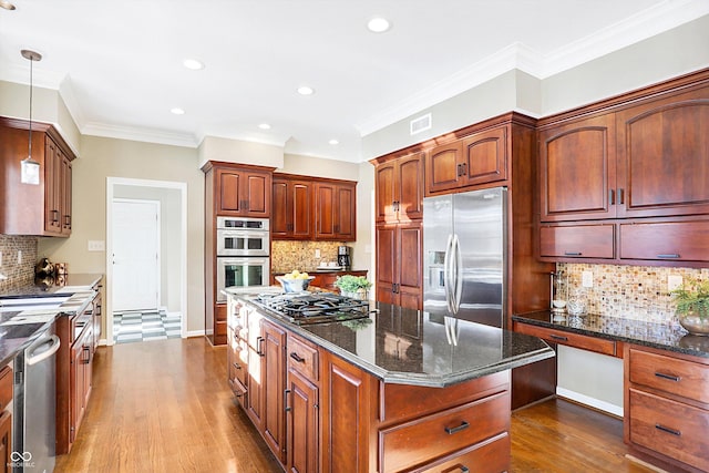 kitchen with hanging light fixtures, appliances with stainless steel finishes, a kitchen island, dark stone counters, and backsplash