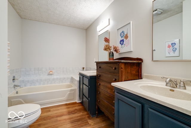 bathroom featuring a bathing tub, a textured ceiling, hardwood / wood-style flooring, toilet, and vanity