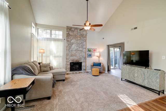 living room featuring a stone fireplace, hardwood / wood-style flooring, high vaulted ceiling, and ceiling fan