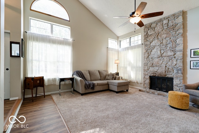 living room with hardwood / wood-style floors, ceiling fan, a textured ceiling, high vaulted ceiling, and a stone fireplace