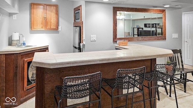 bar featuring sink, tile counters, and stainless steel fridge