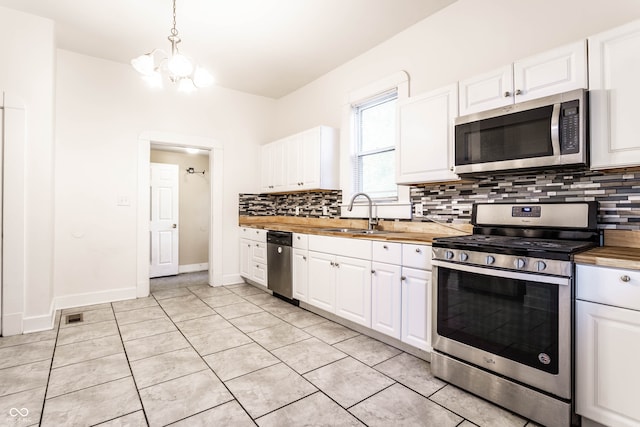 kitchen with wooden counters, stainless steel appliances, sink, decorative light fixtures, and white cabinetry