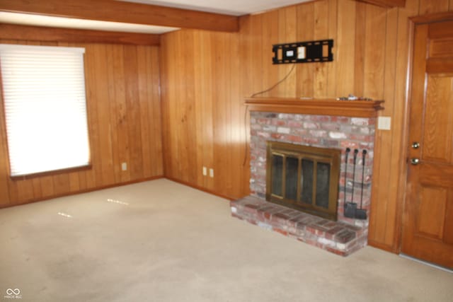 unfurnished living room featuring beamed ceiling, a brick fireplace, light colored carpet, and wood walls