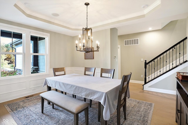 dining room with a chandelier, light wood-type flooring, a tray ceiling, and crown molding