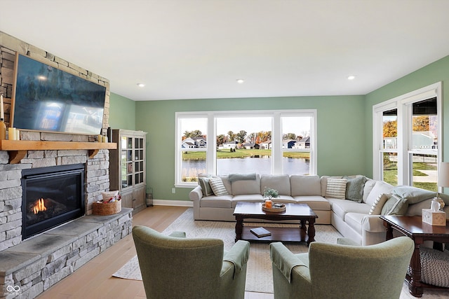 living room featuring a stone fireplace, light wood-type flooring, a water view, and a healthy amount of sunlight